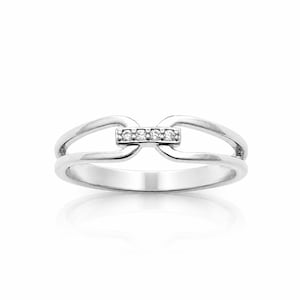 May include: A silver-toned ring featuring a split band design that converges at the center. The central bridge element is set with four small, clear, round-cut stones arranged in a horizontal row, creating a polished and reflective appearance.