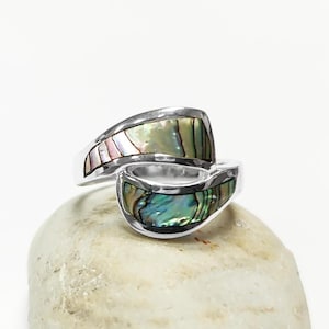 Peut inclure: Une bague en argent avec une incrustation de coquille d'ormeau. La bague présente un design asymétrique unique avec des teintes irisées vertes, bleues et roses. La coquille d'ormeau est sertie dans un anneau en argent poli.