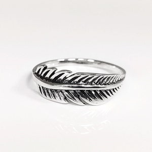 Peut inclure: Une bague en argent avec un motif de plume. La plume est détaillée et a une surface texturée.