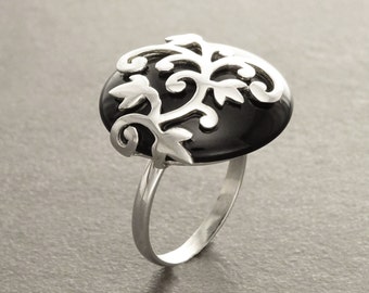 May include: A silver ring with a black onyx stone set in a filigree design. The design features a stylized tree with leaves and branches.