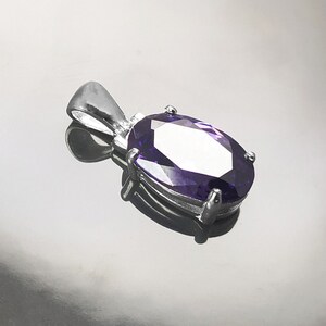 May include: A silver pendant with a large, oval-shaped, purple gemstone.