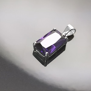 Puede incluir: Un colgante de plata con una piedra preciosa rectangular grande de color púrpura.