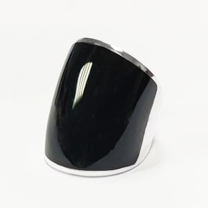 Könnte beinhalten: Ein Ring aus schwarzem Onyx mit einem silbernen Band. Der Ring ist gebogen und hat eine glatte, polierte Oberfläche.