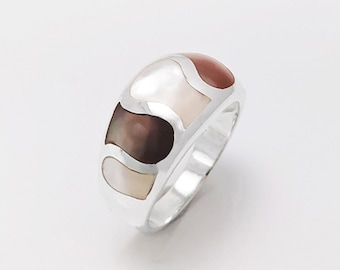 Könnte beinhalten: Ein Silberring mit einem mehrfarbigen Abalone-Muscheleinlege. Der Ring hat ein breites Band und eine glatte, polierte Oberfläche.