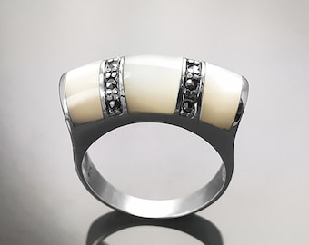 May include: A silver ring with three white mother-of-pearl stones and black marcasite accents.