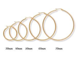 Può includere: Un set di cinque orecchini a cerchio dorati di varie dimensioni, da 30 mm a 70 mm di diametro. Gli orecchini sono esposti su sfondo bianco, con la misura di ogni paio etichettata sotto.