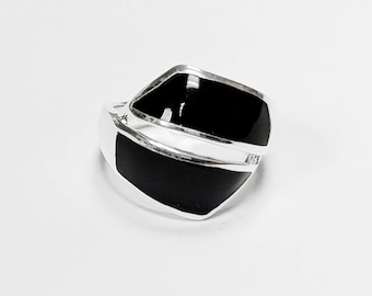 May include: A silver ring with two black enamel geometric shapes. The ring has a modern design with a polished finish. The black enamel contrasts with the silver band, creating a bold and stylish look.