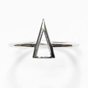 May include: A polished silver-toned ring featuring a prominent, open triangular geometric shape centered on the band. The metal surface is smooth and reflective, showcasing a clean, sharp-edged design that sits upright on the thin circular band.