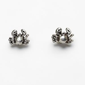 Puede incluir: Una taza de cerámica blanca con un asa negra y el texto "But First, Coffee" en negrita negra. La taza se encuentra sobre un fondo borroso, sugiriendo un ambiente acogedor.