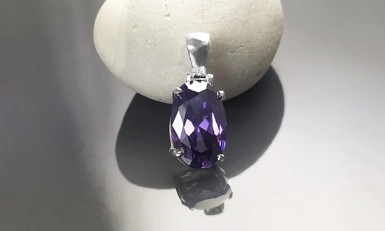 May include: A silver pendant with a large, faceted, oval-shaped purple gemstone.