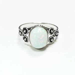 Puede incluir: Anillo de plata con una &oacute;palo blanco ovalado e iridiscente. El anillo tiene detalles florales a ambos lados del &oacute;palo, creando un dise&ntilde;o delicado. El anillo est&aacute; sobre un fondo blanco.