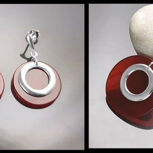 Puede incluir: Un conjunto de pendientes y un colgante de piedra de cornalina roja con detalles plateados. Los pendientes y el colgante presentan un dise&ntilde;o redondo y en capas con un c&iacute;rculo plateado en el centro.