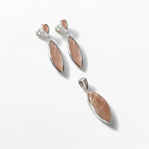 May include: A jewelry set consisting of two drop earrings and one pendant. Each piece features a marquise-shaped, iridescent peach-colored stone set in a polished silver-tone metal frame. The earrings have post backs, and the pendant has a bail.