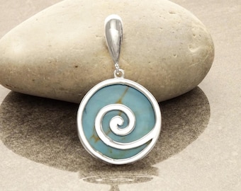 Puede incluir: Un colgante de plata con un diseño de espiral azul y blanco. El colgante es redondo y tiene una anilla de plata.