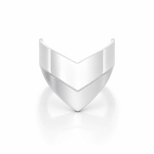 May include: A polished silver ring featuring a wide, V-shaped chevron design. The band has a smooth, reflective metallic surface that tapers to a point at the centre, creating a sharp, angular silhouette that wraps around the finger.