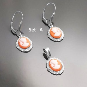 May include: Set A of silver earrings and a pendant featuring a cameo design with a white profile on an orange background. The earrings have a lever back closure.