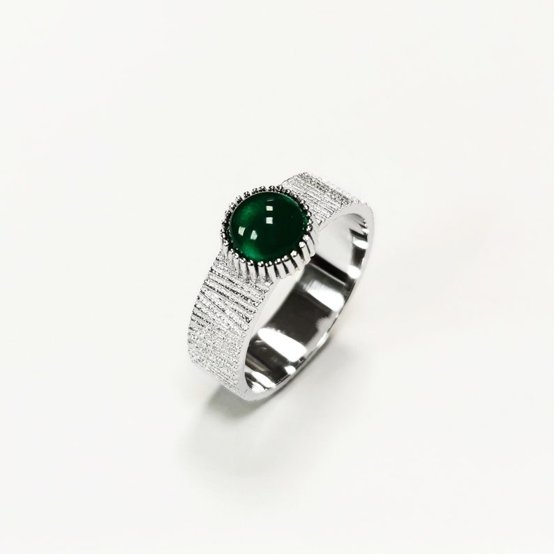 Puede incluir: Un anillo de plata con una banda texturizada y una piedra preciosa verde engastada en un engaste de plata.