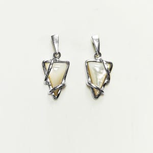 May include: A pair of silver-toned pendants featuring a triangular-shaped iridescent white shell inlay. Each pendant is encased in a polished metal frame that wraps around the edges of the triangle, topped with a simple triangular bail for hanging.