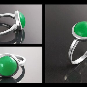 May include: A silver ring featuring a large, round, bright green stone. The stone is set in a bezel setting, and the band is a simple, polished silver. The ring is displayed in multiple views against a dark background.