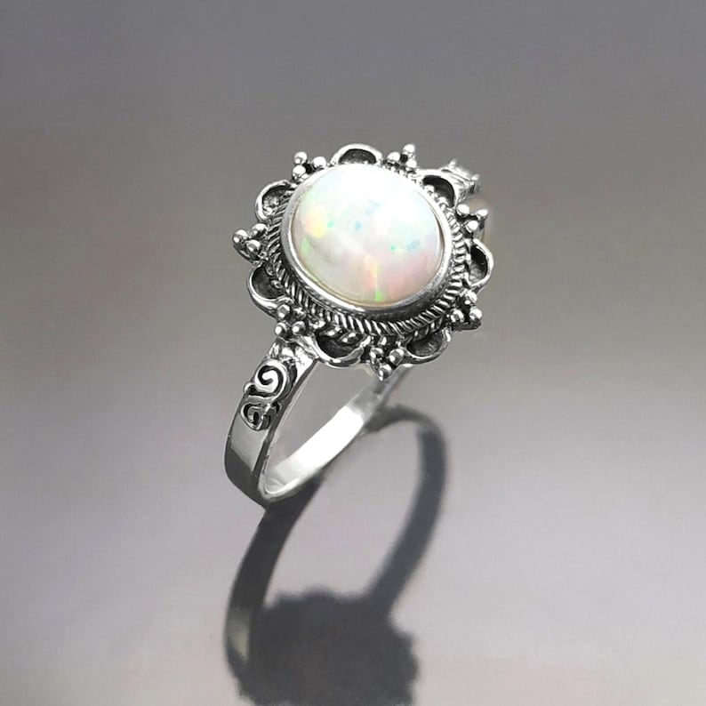Puede incluir: Anillo de plata con una gran piedra de &oacute;palo ovalada. El &oacute;palo tiene un aspecto blanco lechoso con destellos iridiscentes. El anillo tiene un dise&ntilde;o de filigrana ornamentado alrededor de la piedra y en la banda, de estilo vintage o antiguo.