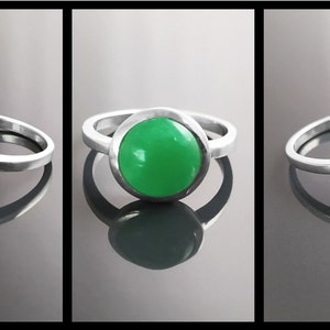 May include: A silver ring with a large, round, bright green stone. The stone is set in a bezel setting, and the band is a simple, polished silver. The ring is displayed in three different angles.