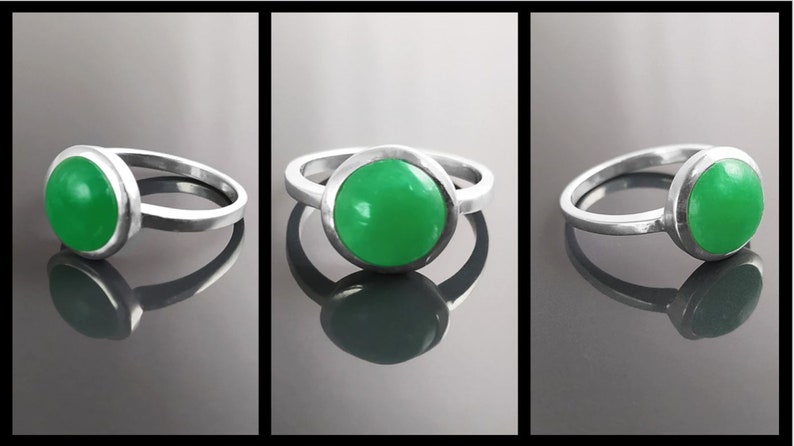 May include: A silver ring with a large, round, bright green stone. The stone is set in a bezel setting, and the band is a simple, polished silver. The ring is displayed in three different angles.