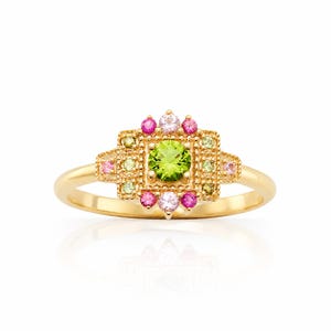 Könnte beinhalten: Ein goldener Ring mit einem quadratischen, hellgrünen Edelstein in der Mitte, umgeben von kleineren rosa, weißen und hellgrünen Edelsteinen. Der Ring hat ein detailliertes, verziertes Design mit poliertem Finish.