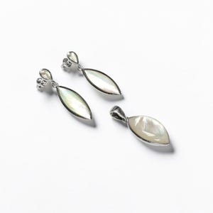 May include: A pair of silver drop earrings and a matching pendant, each featuring an elongated marquise-shaped inlay of iridescent white mother-of-pearl. The metal settings are polished silver, with the earrings using a post-back closure.