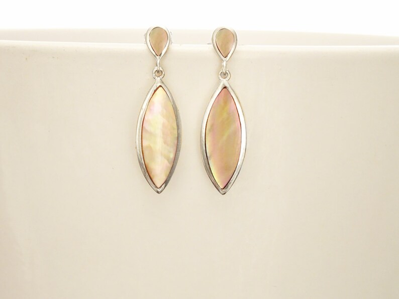 May include: A pair of drop earrings featuring marquise-shaped iridescent shell inlays set in silver-toned metal. Each earring consists of a small teardrop-shaped top piece connected by a jump ring to a larger, elongated marquise-shaped pendant.
