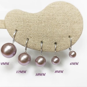 Op de afbeelding: Vijf zilveren oorbellen met klapoorbel en ronde, glanzende lavendelkleurige parels in oplopende maten. De parels zijn gelabeld met hun respectievelijke diameters: 14MM, 12MM, 10MM, 8MM en 6MM, gerangschikt op een beige display met textuur.