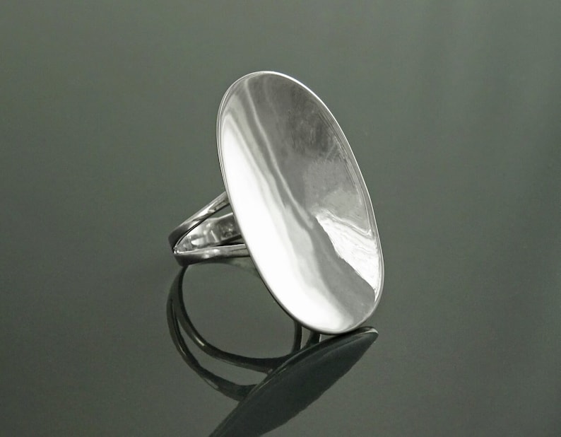 K&ouml;nnte beinhalten: Ein silberner Ring mit einer gro&szlig;en, ovalen Oberseite. Die Oberseite des Rings ist glatt und hat eine leichte W&ouml;lbung.