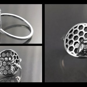 Op de afbeelding: Een zilveren ring met een bij en honingraat ontwerp. De honingraat is een cirkel met een bij in het midden. De ring ligt op een grijze achtergrond.