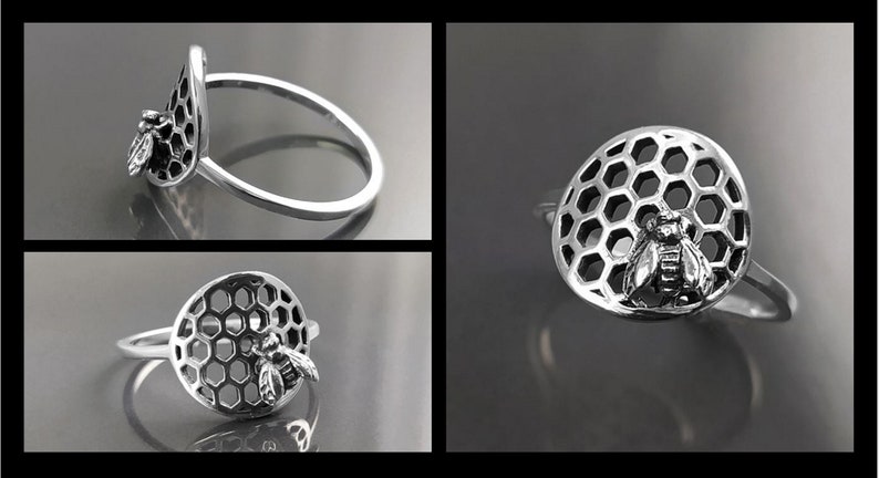 Op de afbeelding: Een zilveren ring met een bij en honingraat ontwerp. De honingraat is een cirkel met een bij in het midden. De ring ligt op een grijze achtergrond.
