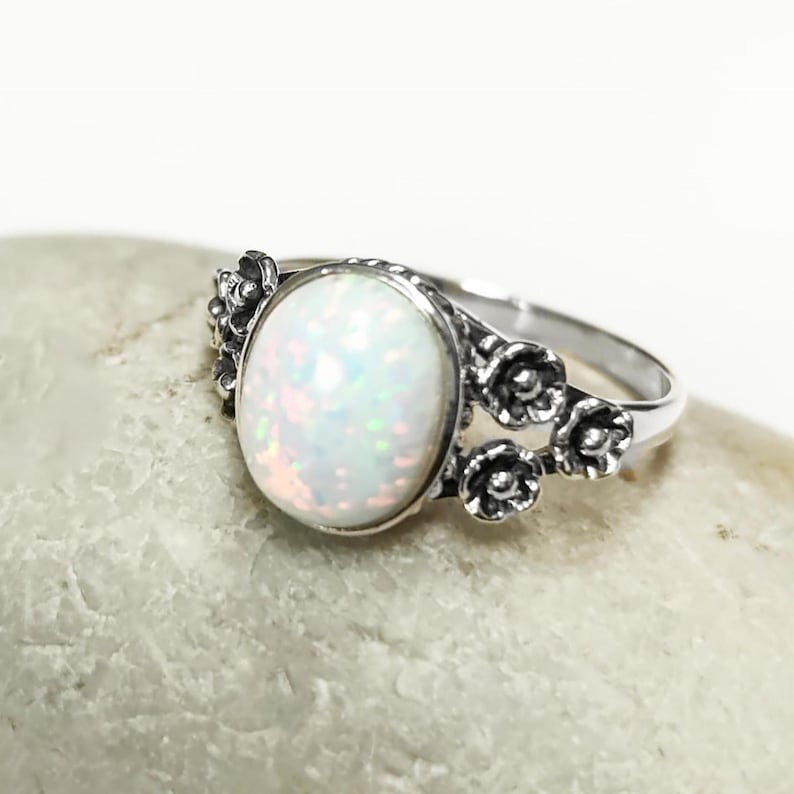 Puede incluir: Anillo de plata con una piedra de &oacute;palo ovalada e iridiscente. El &oacute;palo tiene una base blanca lechosa con destellos de color. El anillo est&aacute; adornado con peque&ntilde;os detalles florales.