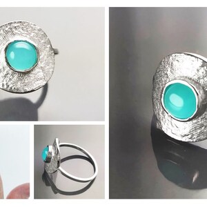 May include: A silver ring with a textured, circular band and a turquoise gemstone set in the center.