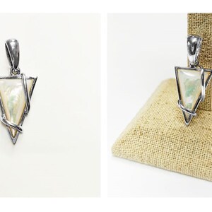 May include: A triangular pendant featuring a polished silver-tone metal frame that wraps around a smooth, iridescent white mother-of-pearl inlay. The pendant includes a sturdy silver-tone bail at the top for attachment to a chain or cord.