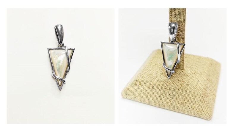 May include: A triangular pendant featuring a polished silver-tone metal frame that wraps around a smooth, iridescent white mother-of-pearl inlay. The pendant includes a sturdy silver-tone bail at the top for attachment to a chain or cord.
