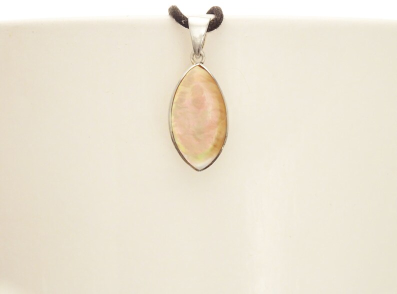 May include: A marquise-shaped pendant featuring an iridescent, pale pink and cream-colored shell inlay set within a polished silver-toned metal frame. The pendant is suspended from a dark brown cord, showcasing a smooth, reflective surface.