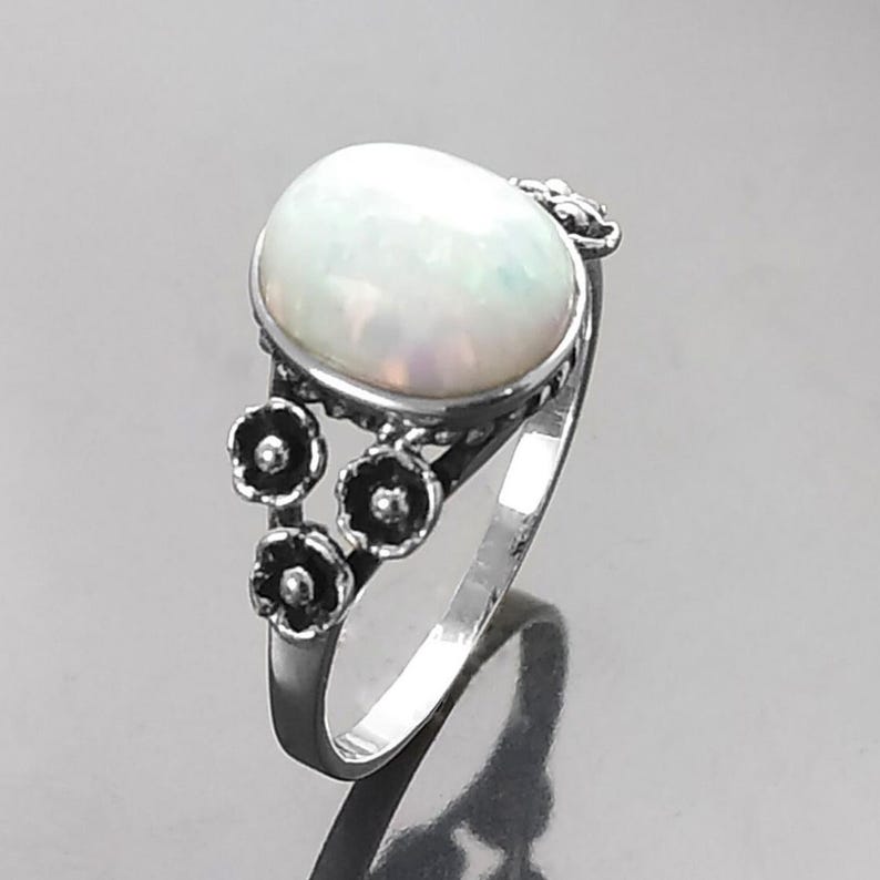 Puede incluir: Anillo de plata con una gran piedra de &oacute;palo ovalada. El &oacute;palo es blanco lechoso con destellos iridiscentes. El anillo tiene peque&ntilde;os detalles florales oscuros en la banda. Una joya.