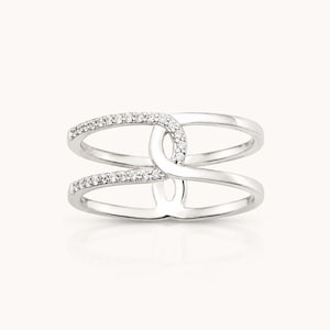 May include: A silver-toned ring featuring a double-band design that converges at the centre. The top and bottom bands are accented with small, clear, round-cut stones set along the outer edges, creating a symmetrical and open-work appearance.