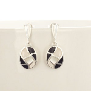 Peut inclure: Une paire de boucles d'oreilles pendantes en argent avec des incrustations ovales noires et blanches. Les incrustations sont en nacre et onyx noir.