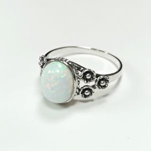 Puede incluir: Anillo de plata con una piedra de &oacute;palo ovalada e iridiscente. El anillo est&aacute; adornado con detalles florales en la banda, a&ntilde;adiendo un toque delicado. El &oacute;palo muestra un juego de colores. Una joya.