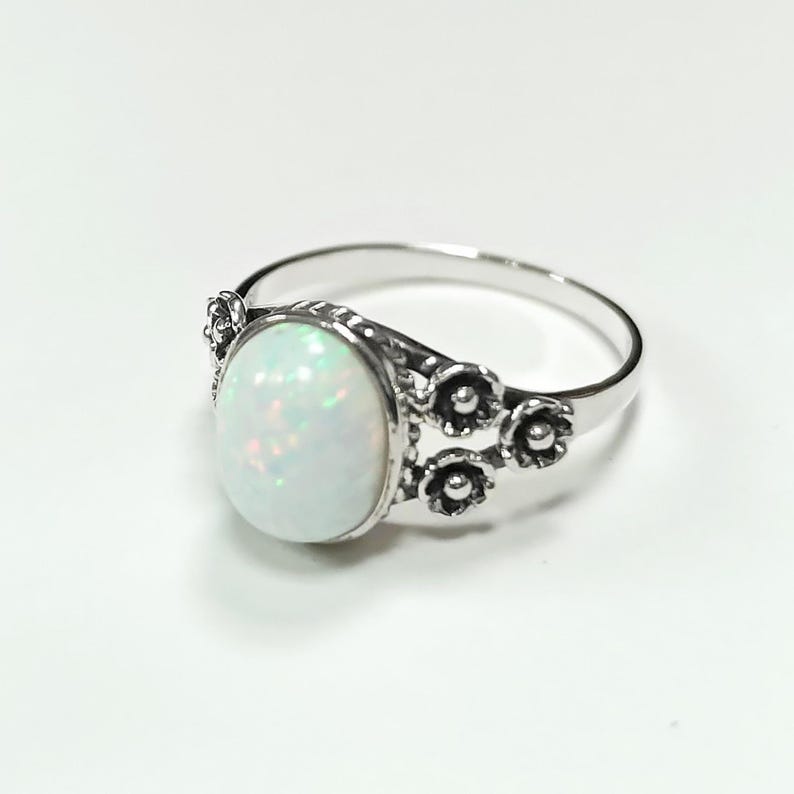 Puede incluir: Anillo de plata con una piedra de &oacute;palo ovalada e iridiscente. El anillo est&aacute; adornado con detalles florales en la banda, a&ntilde;adiendo un toque delicado. El &oacute;palo muestra un juego de colores. Una joya.