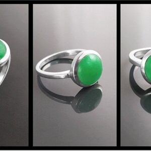 May include: A sterling silver ring with a bright green, round gemstone. The gemstone is set in a bezel setting, and the ring has a simple, elegant design. The ring is displayed in three different views.