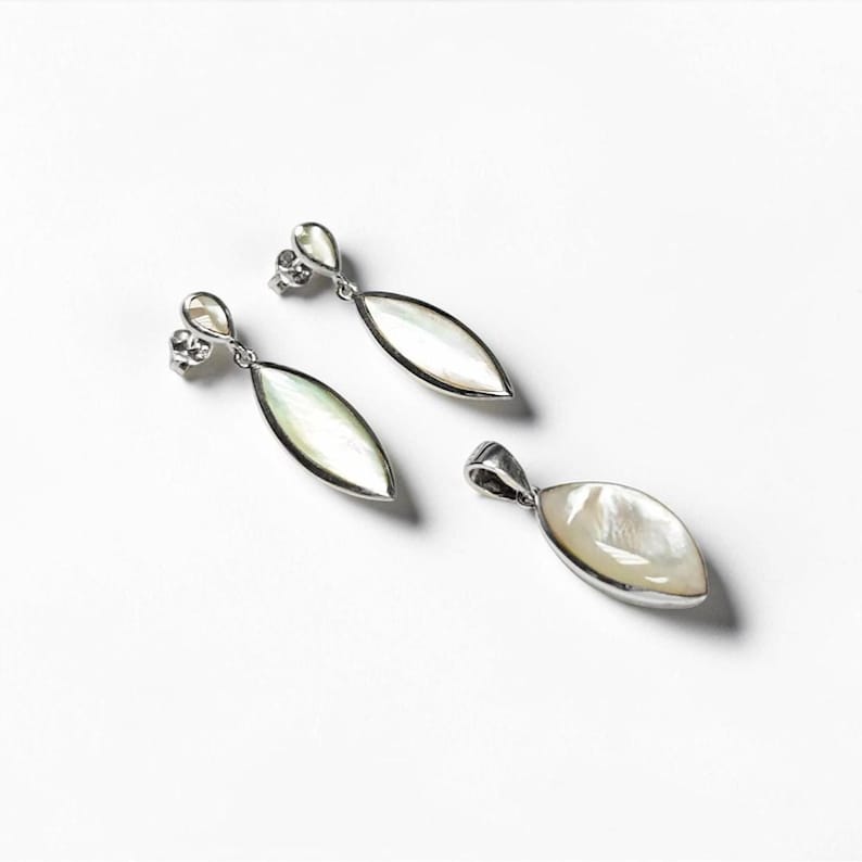 May include: A pair of silver drop earrings and a matching pendant, each featuring a marquise-shaped iridescent mother-of-pearl inlay set in a polished silver frame. The earrings have post backs, and the pendant includes a silver bail for hanging.