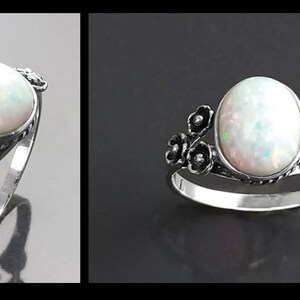 Puede incluir: Anillo de plata con una gran piedra de &oacute;palo ovalada. El &oacute;palo tiene un aspecto blanco lechoso con destellos iridiscentes. El anillo est&aacute; adornado con peque&ntilde;os detalles florales oscuros en los laterales, a&ntilde;adiendo un toque delicado a la joya.
