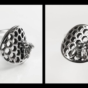 Op de afbeelding: Een zilveren ring met een bij- en honingraatontwerp. De bij is geplaatst op de honingraat, die een uitgesneden ontwerp is.