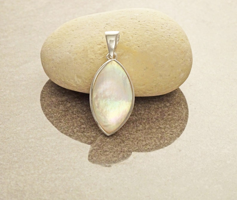 May include: A marquise-shaped pendant featuring an iridescent mother-of-pearl inlay set within a polished silver-toned metal frame. The pendant includes a tapered silver-toned bail at the top for attachment to a chain or cord necklace.
