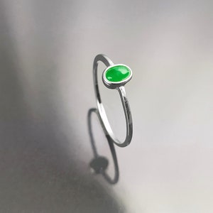 May include: A silver ring with a small oval-shaped green gemstone.