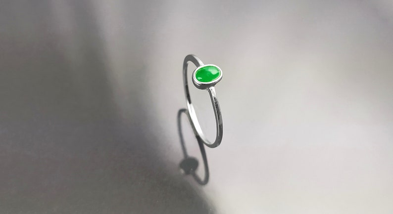 May include: A silver ring with a small oval-shaped green gemstone.
